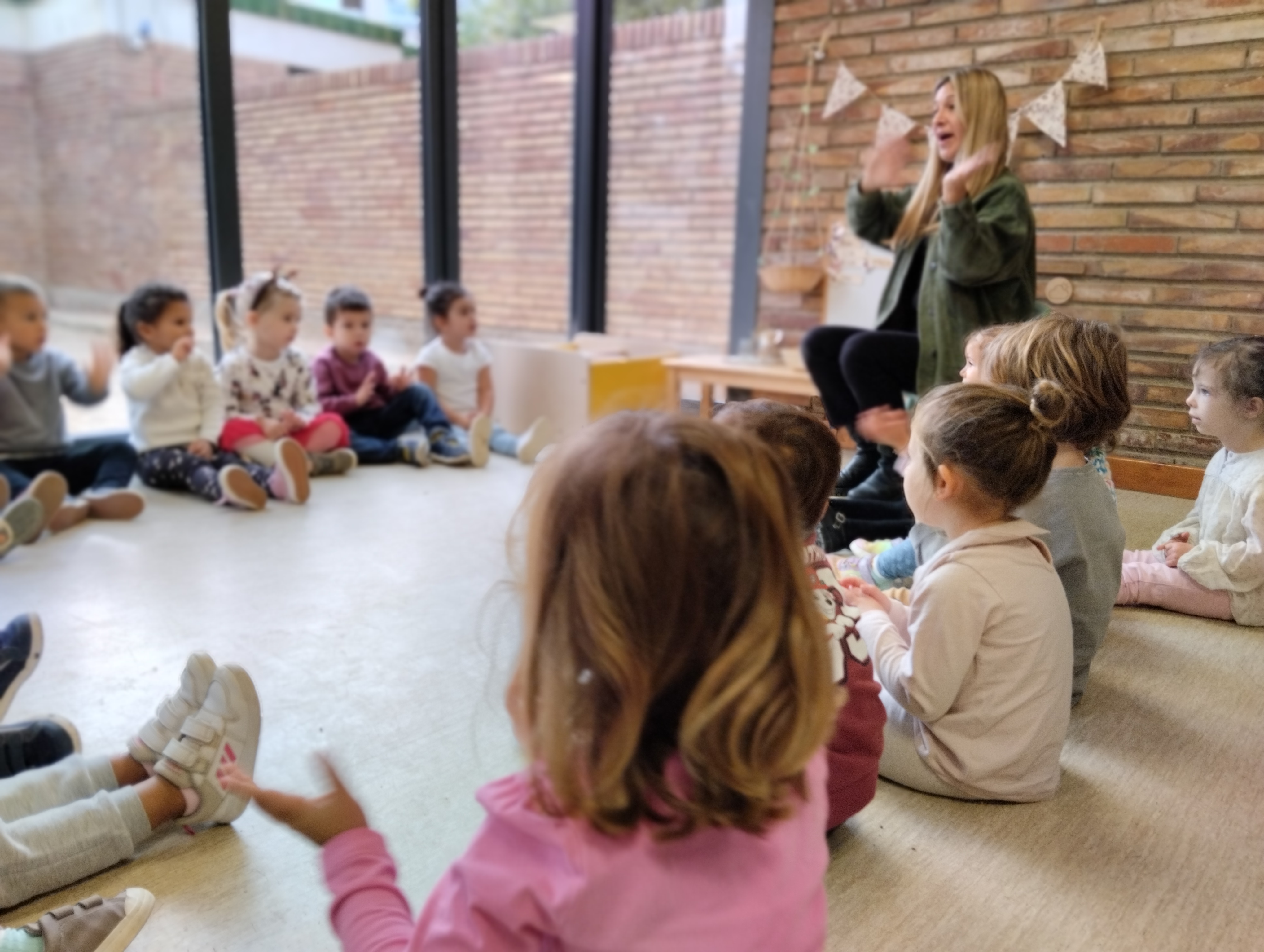 Un cercle d'infants asseguts a terra en cercle, escoltant a la mestra