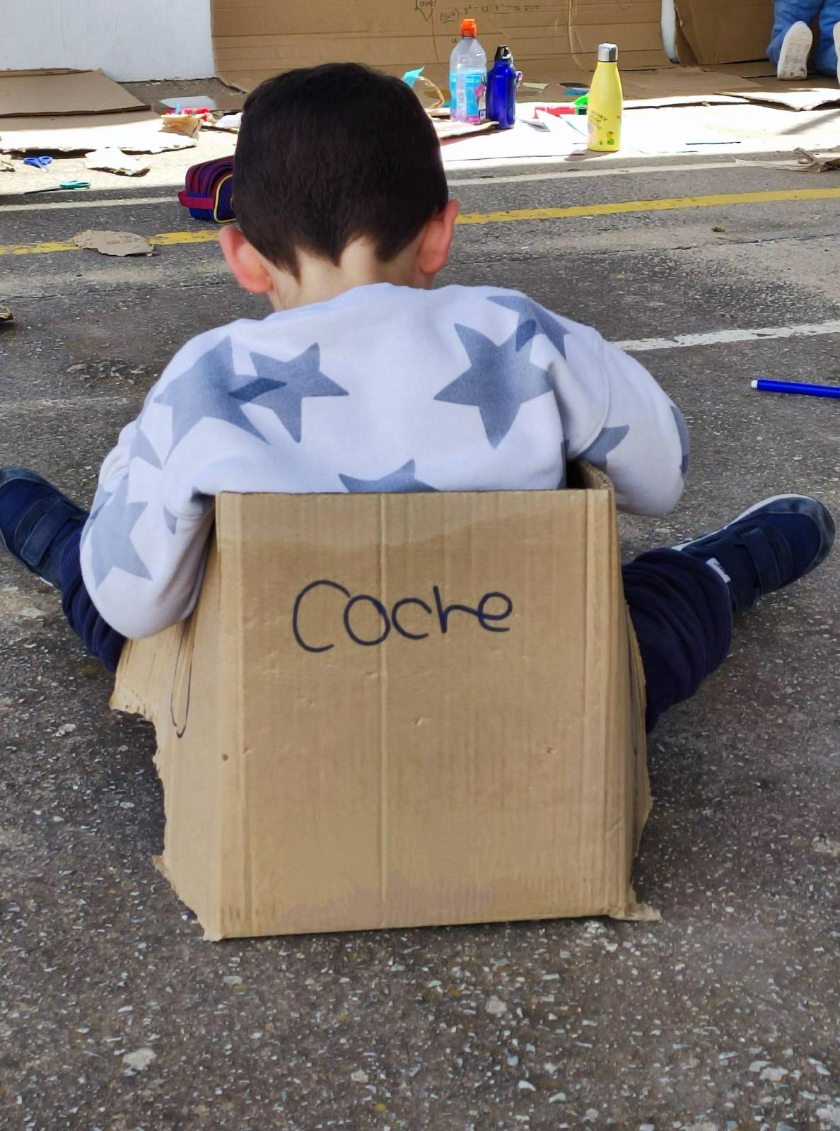 Un niño dentro de una caja de cartón con la palabra escrita "coche" en la parte trasera de la caja